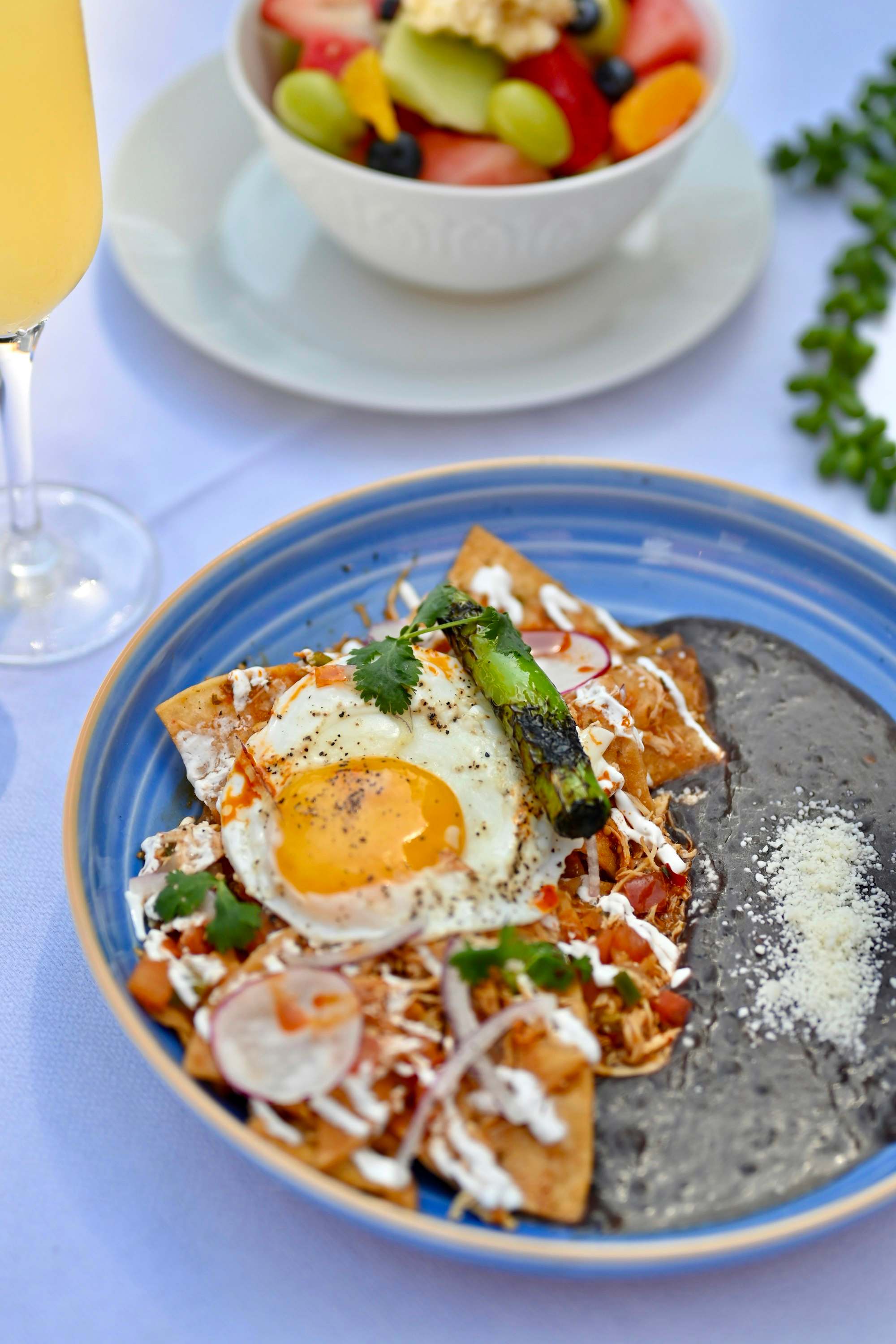 Chilaquiles con huevo estrellado, crema y frijoles en un plato azul