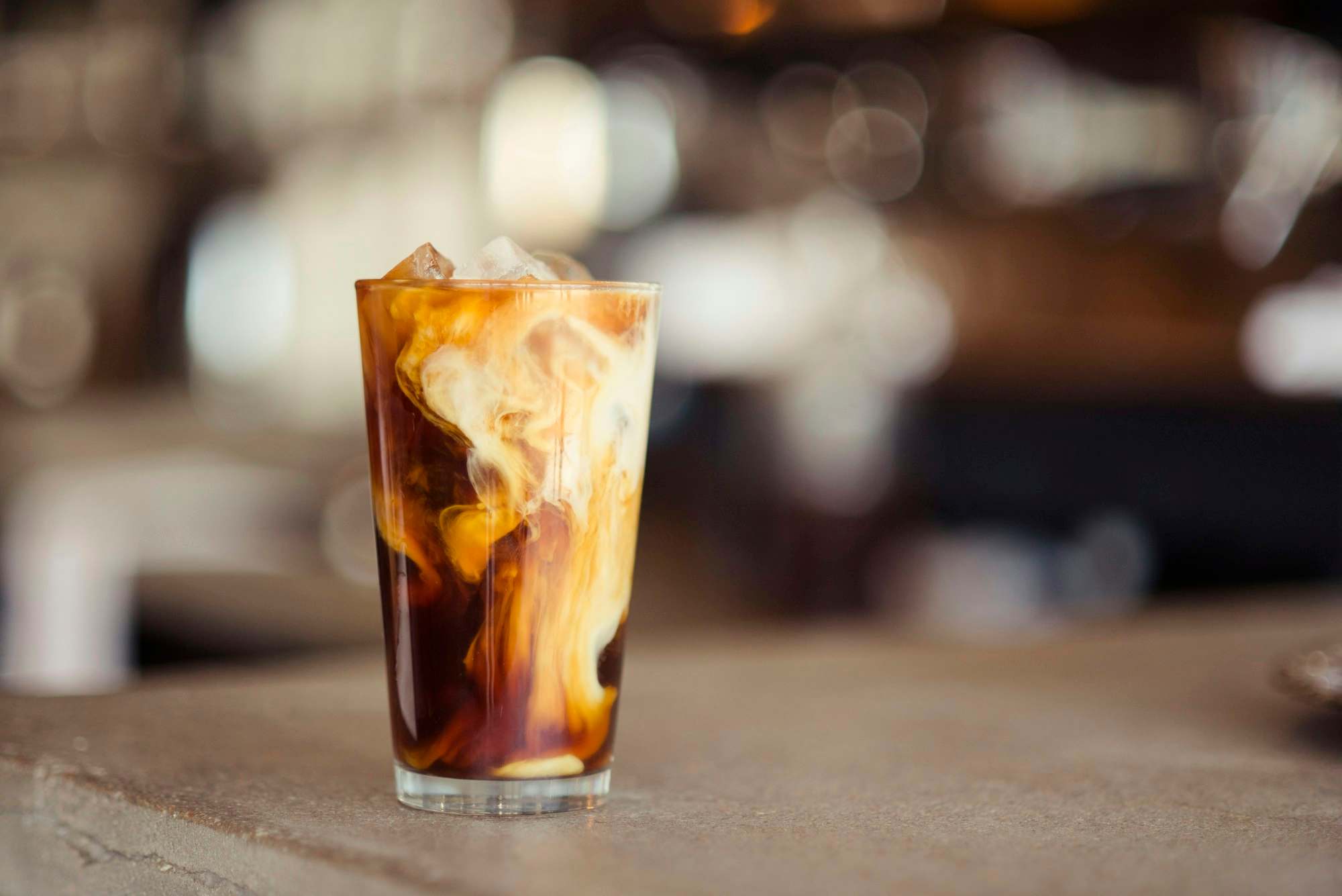 Vaso alto con bebida fría, hielo y leche en una barra de madera