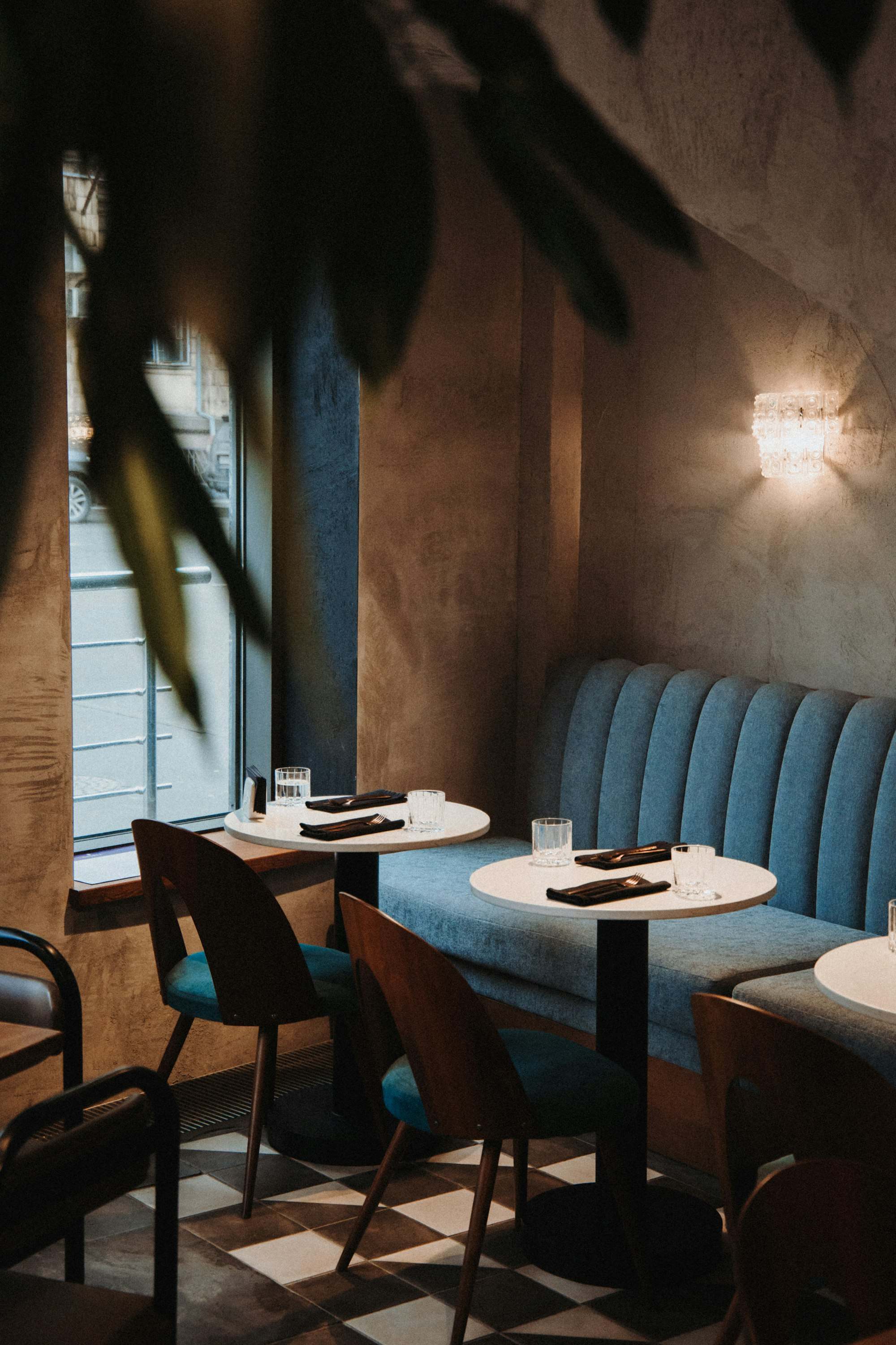 Salón con sillones azules, mesas redondas y luz cálida de pared