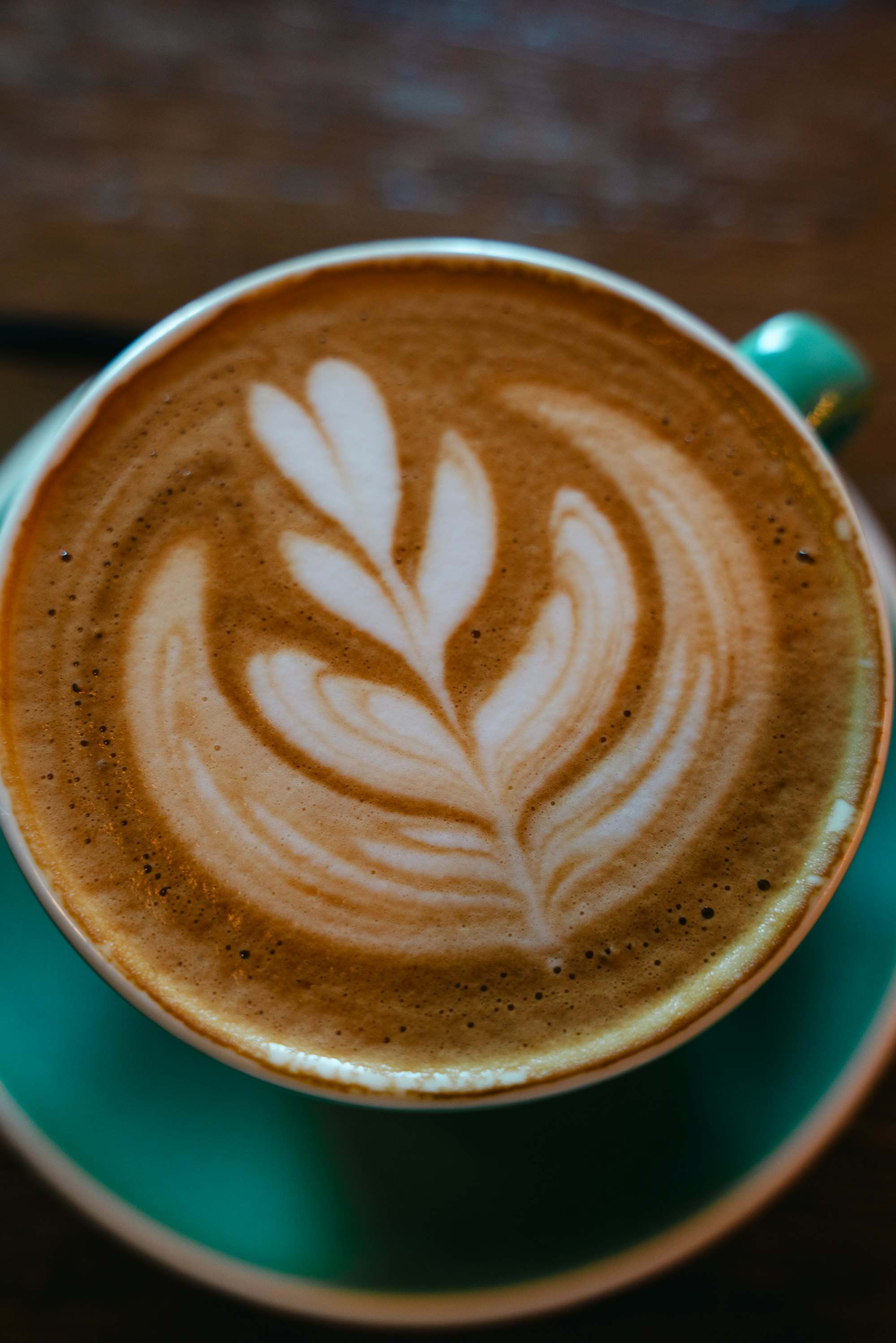 Latte con arte en forma de hoja en una taza verde azulada