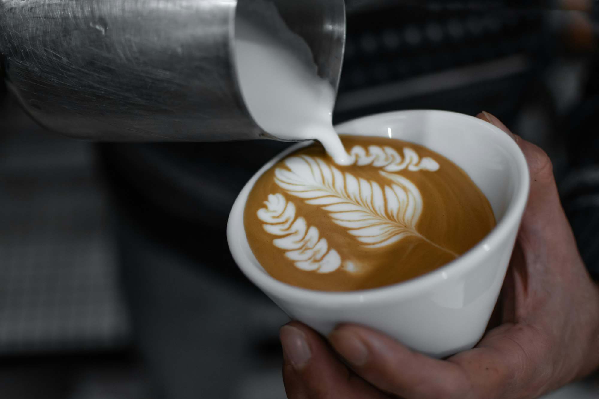 Manos sosteniendo un capuchino con arte latte en forma de hoja
