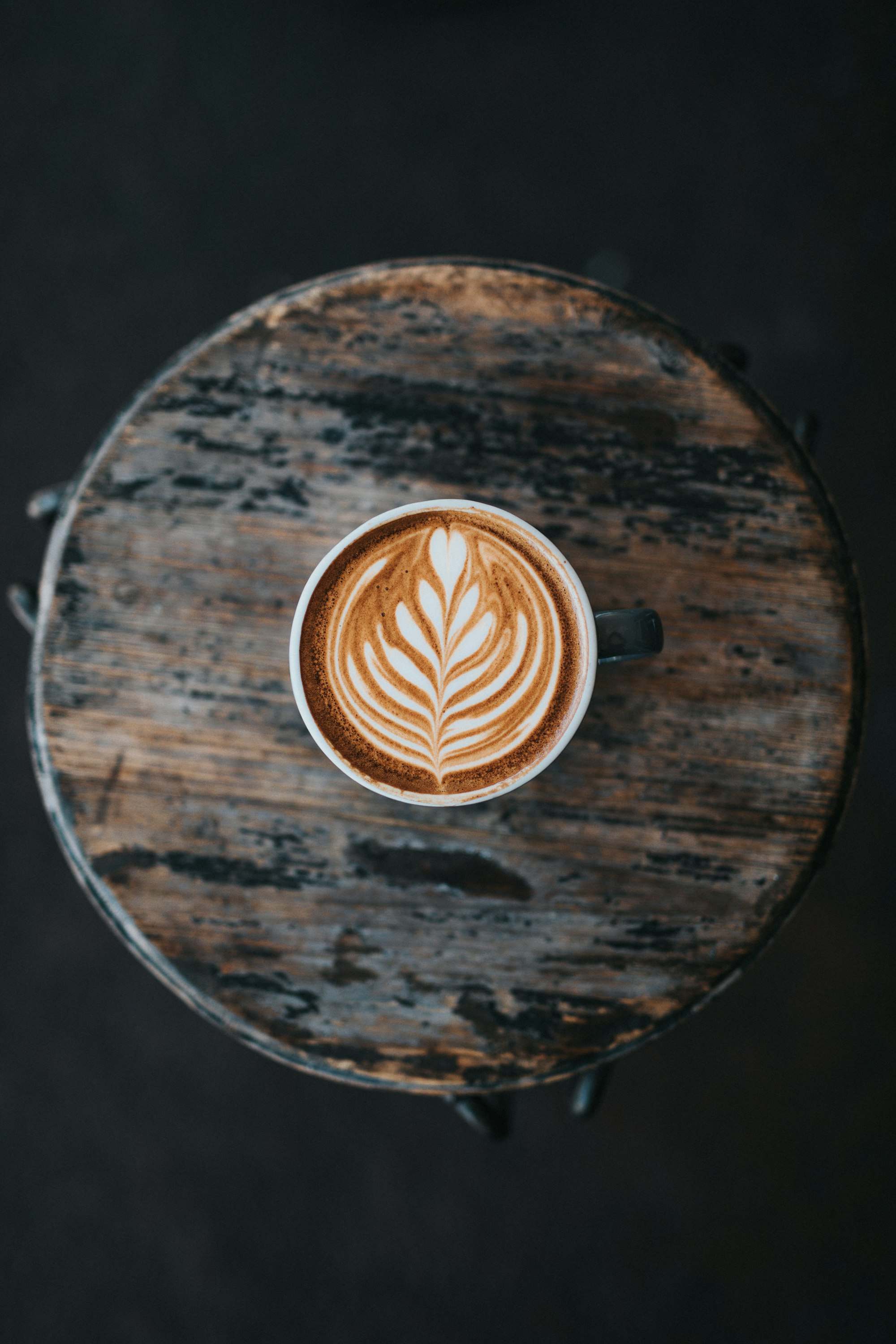 Capuchino con roseta en una mesa de madera oscura y desgastada