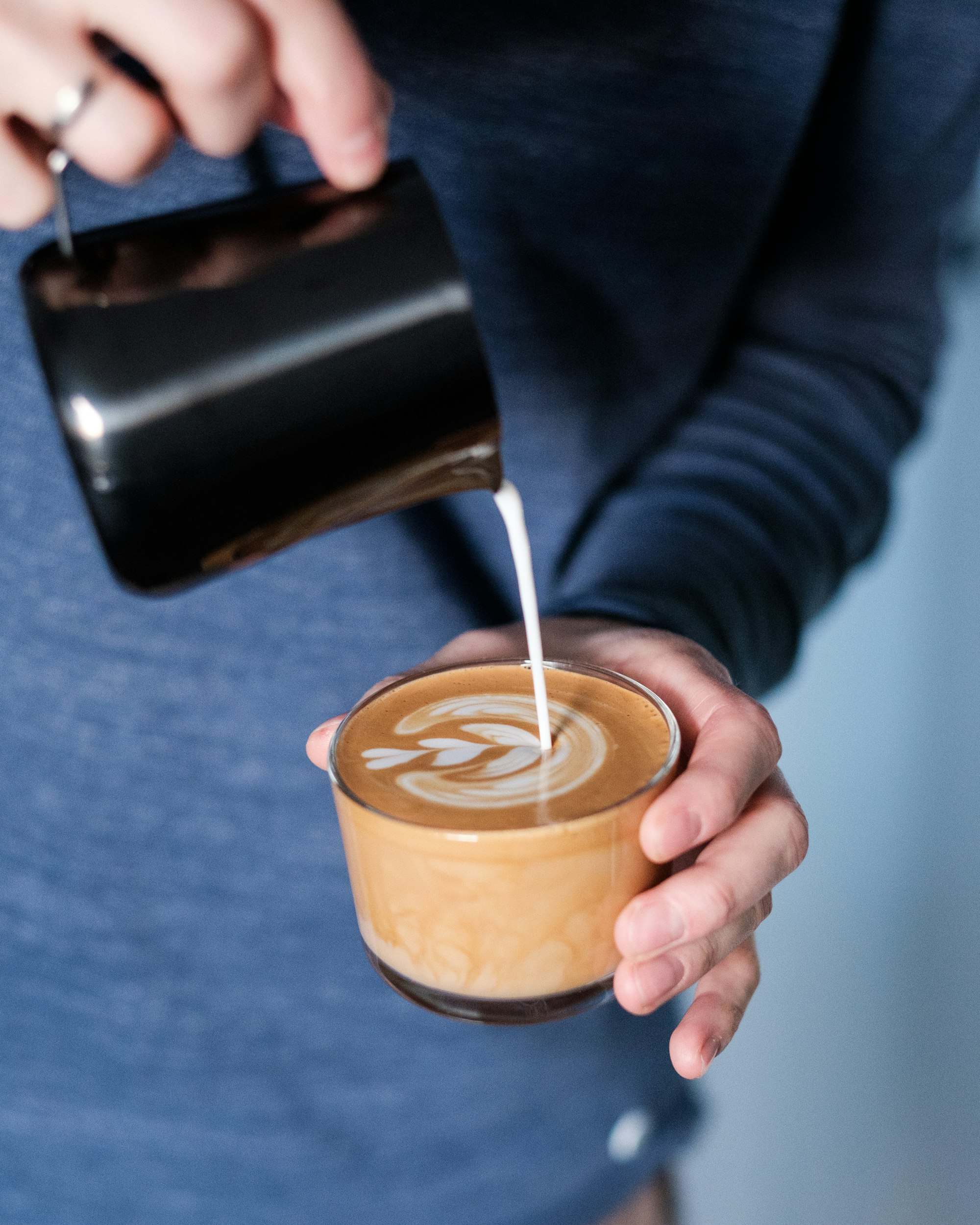 Manos vertiendo leche texturizada en una taza para hacer arte latte