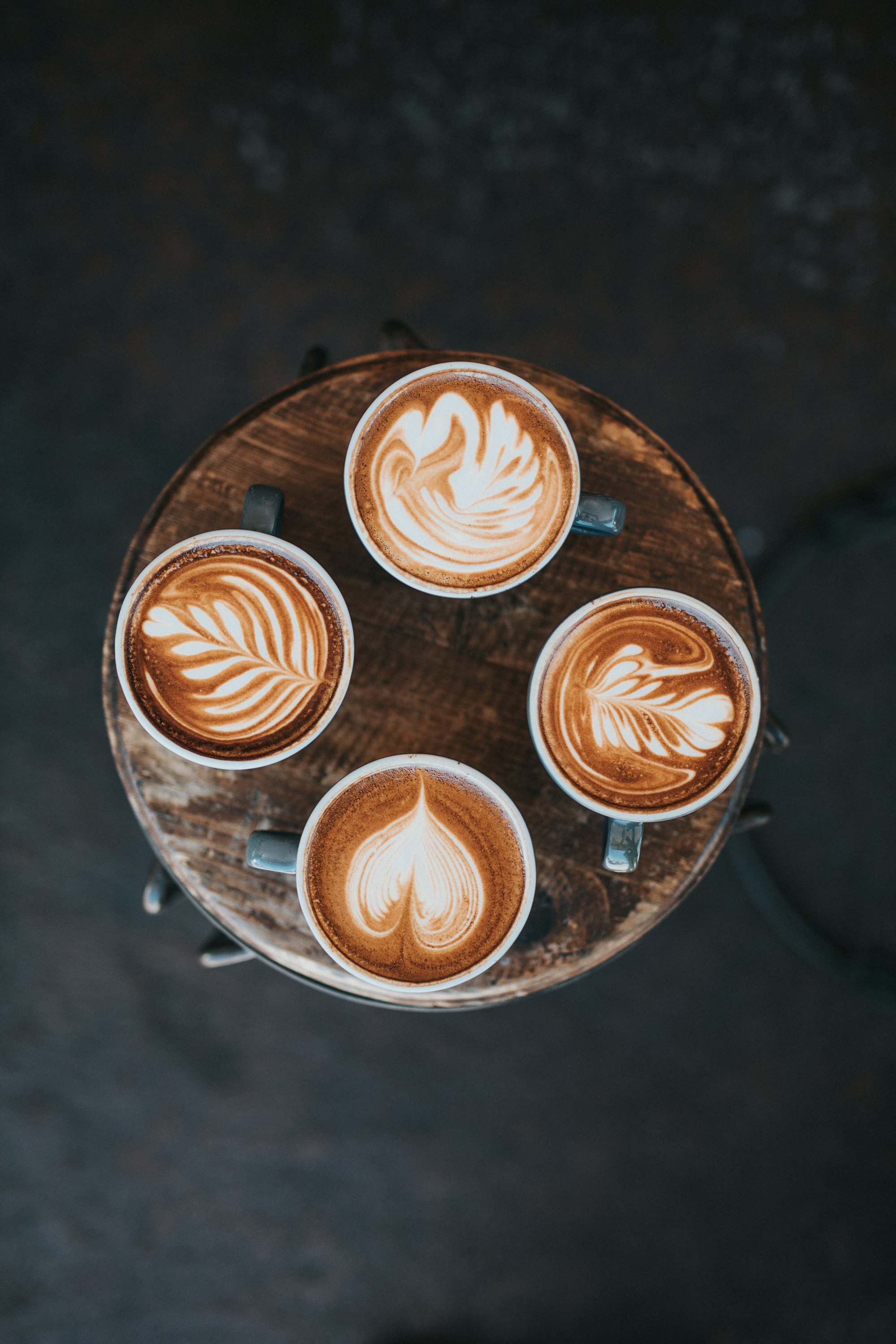 Cuatro capuchinos con arte latte sobre una mesa redonda de madera